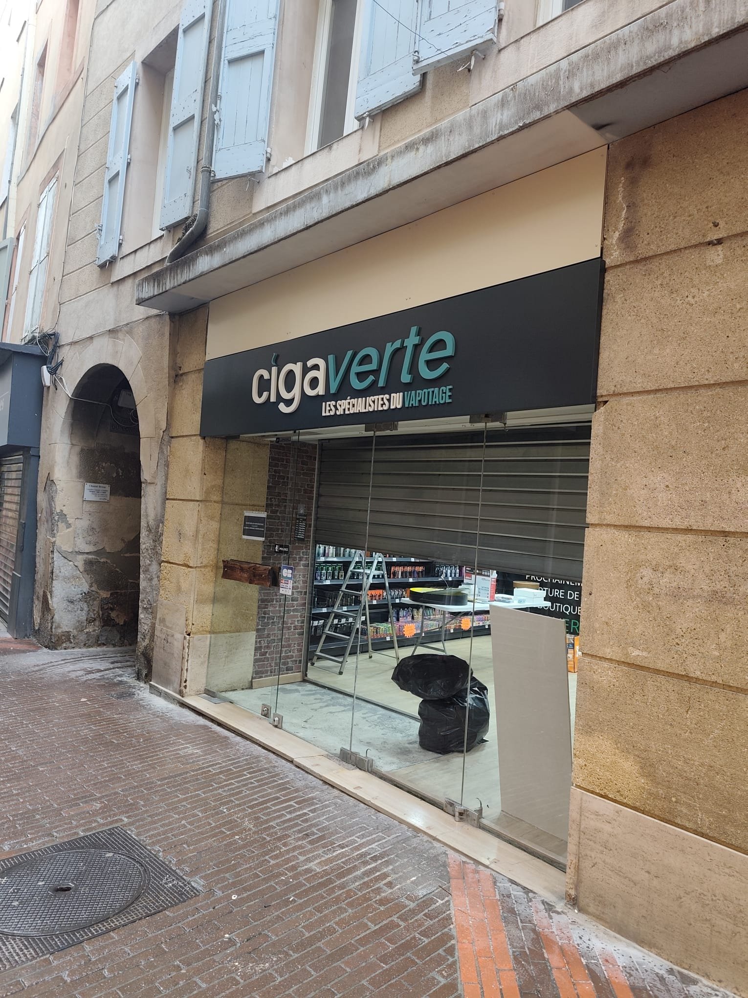 Façade Ciga Verte à Manosque vue depuis le passage voûté voisin, bandeau noir au-dessus de la vitrine