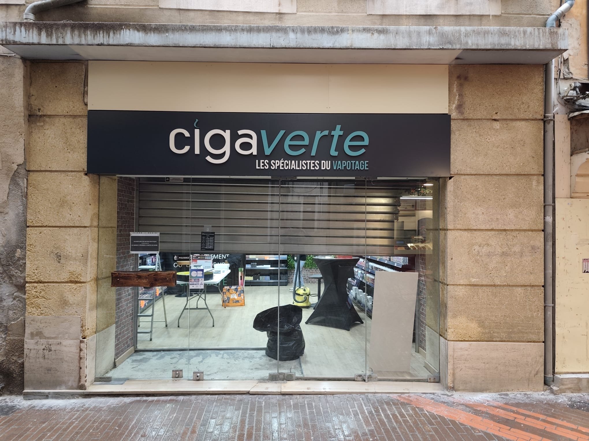 Boutique Ciga Verte dans une rue piétonne du centre ancien de Manosque : bandeau noir avec lettres en relief blanches et vertes, entre deux piliers en pierre