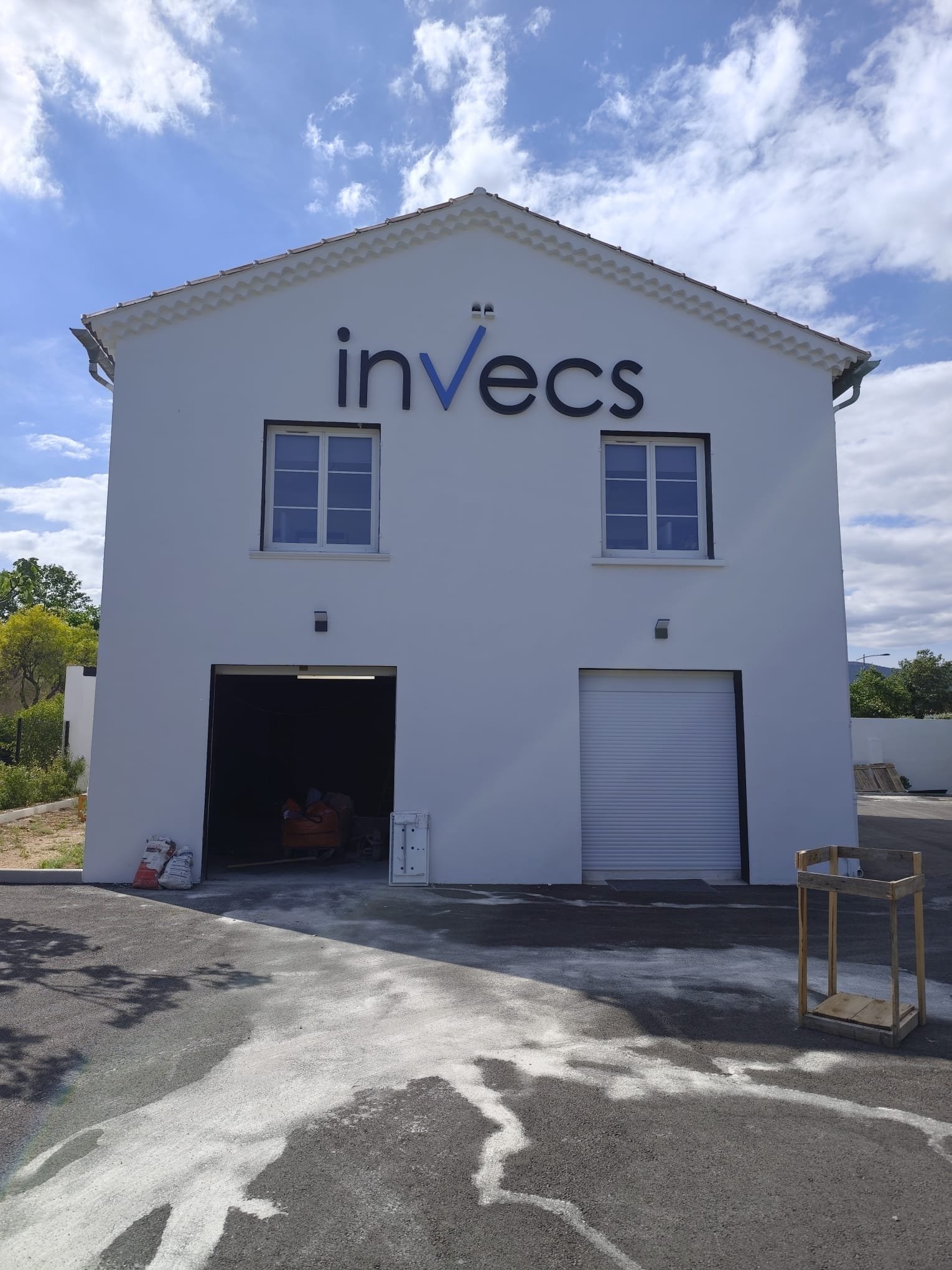 Lettres boîtier Invecs noires avec le V bleu, en haut du pignon blanc d'un bâtiment à Cuers