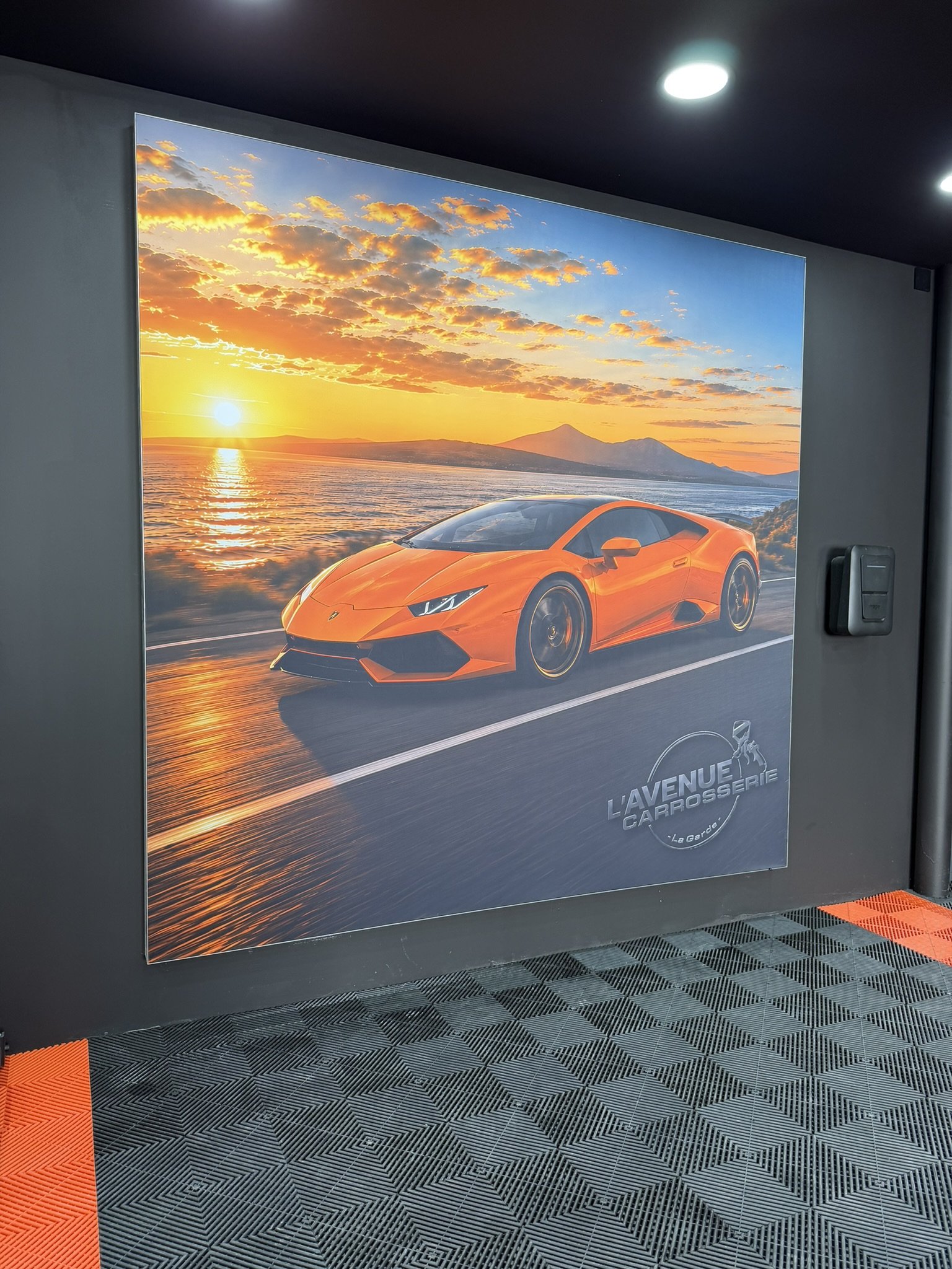 Caisson rétroéclairé en toile tendue : voiture orange au coucher du soleil, dans L'Avenue Carrosserie à La Garde