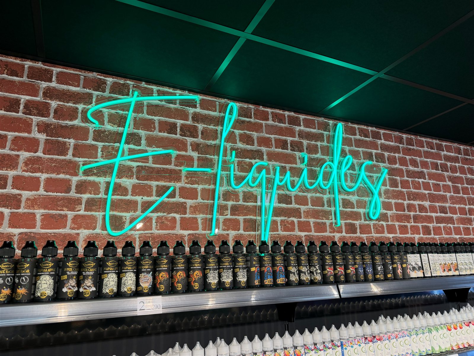 Néon LED E-liquides en écriture manuscrite verte sur un mur de briques, au-dessus des présentoirs