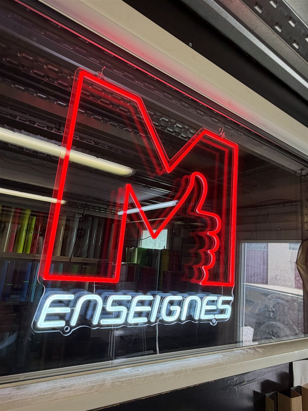 Néon M Enseignes vu de biais derrière la vitrine de l'atelier
