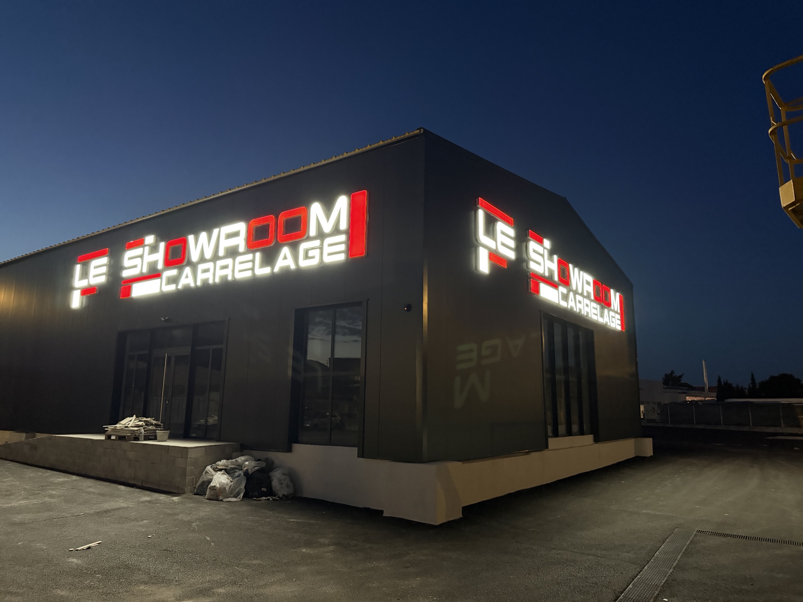 Les deux enseignes en lettres boîtier lumineuses rouges et blanches du Showroom Carrelage allumées de nuit, à La Farlède