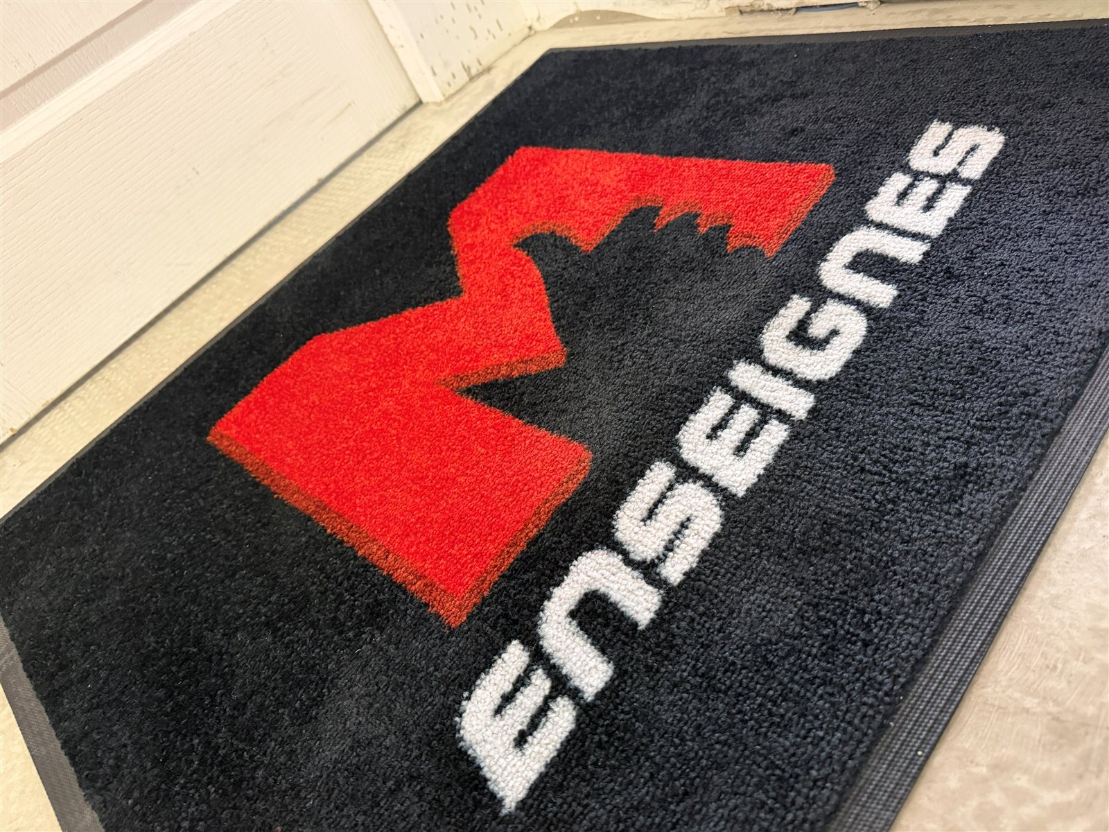 Gros plan sur le velours du tapis au logo M Enseignes : M rouge et lettres blanches